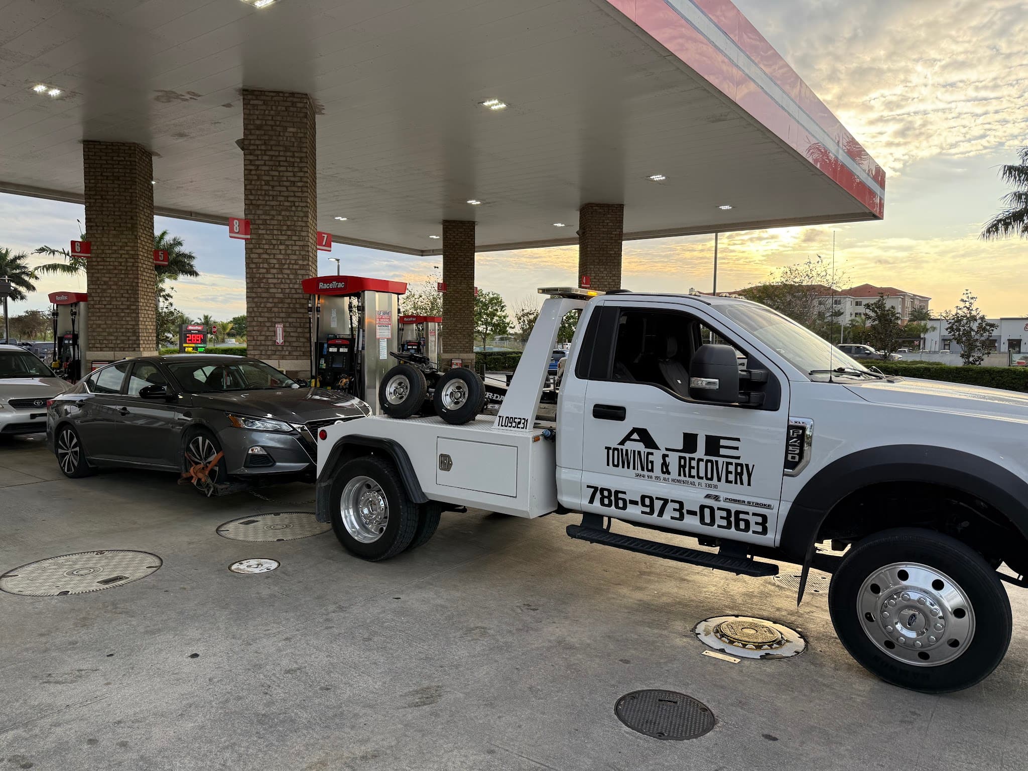 AJE Towing & Recovery flatbed truck loading a car at a South Florida gas station